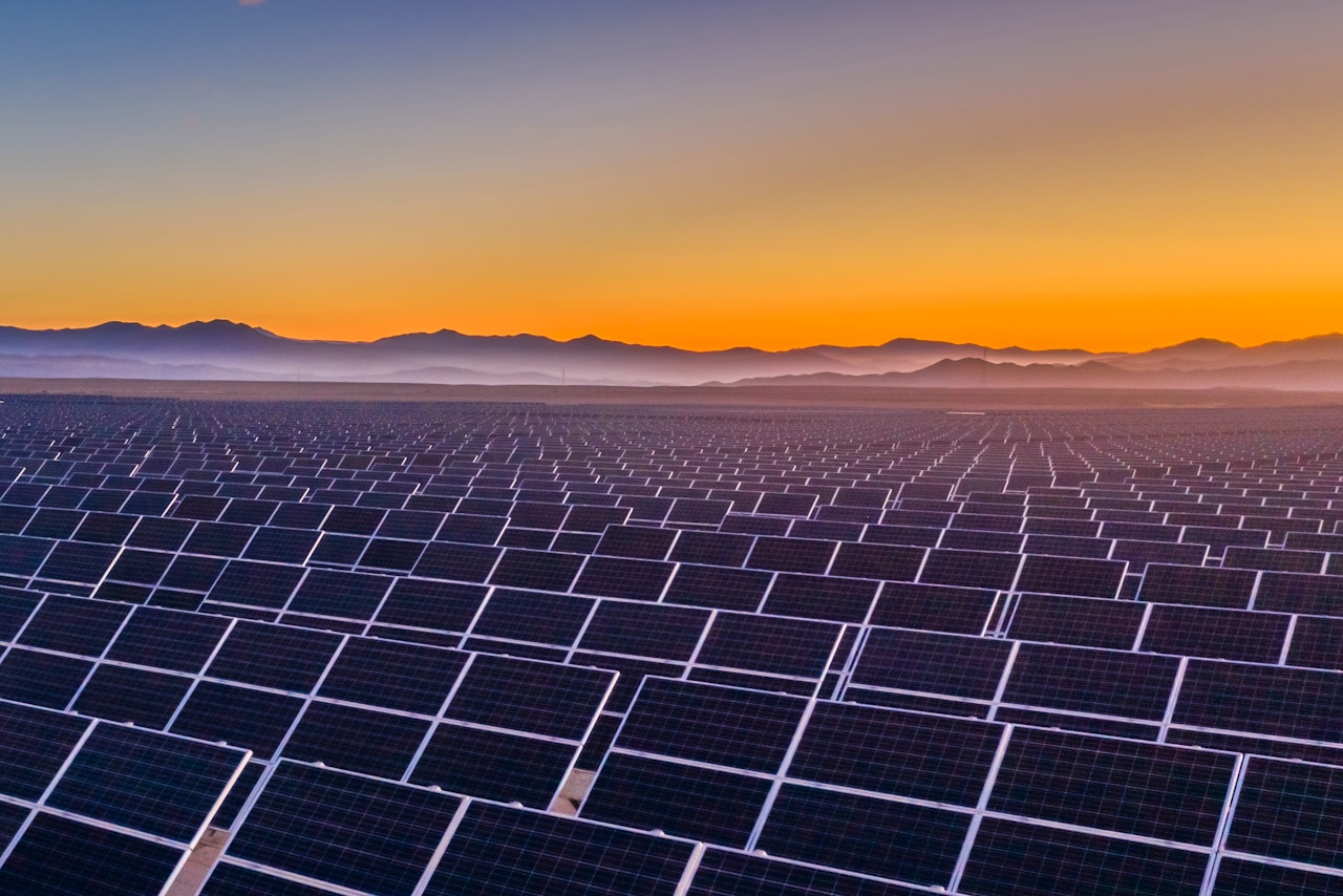 Photo depicts and aerial view of hundreds solar energy panels rows along the dry lands at Atacama Desert, Chile. Huge Photovoltaic PV Plant in the middle of the desert from an aerial drone point of view during sunset